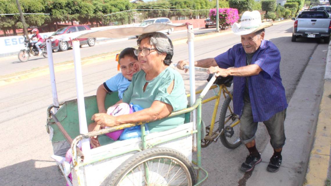 Juan Rendón y Susana Zamora llevan a su nieta María Natali a la escuela en un triciclo acondicionado por el abuelo.