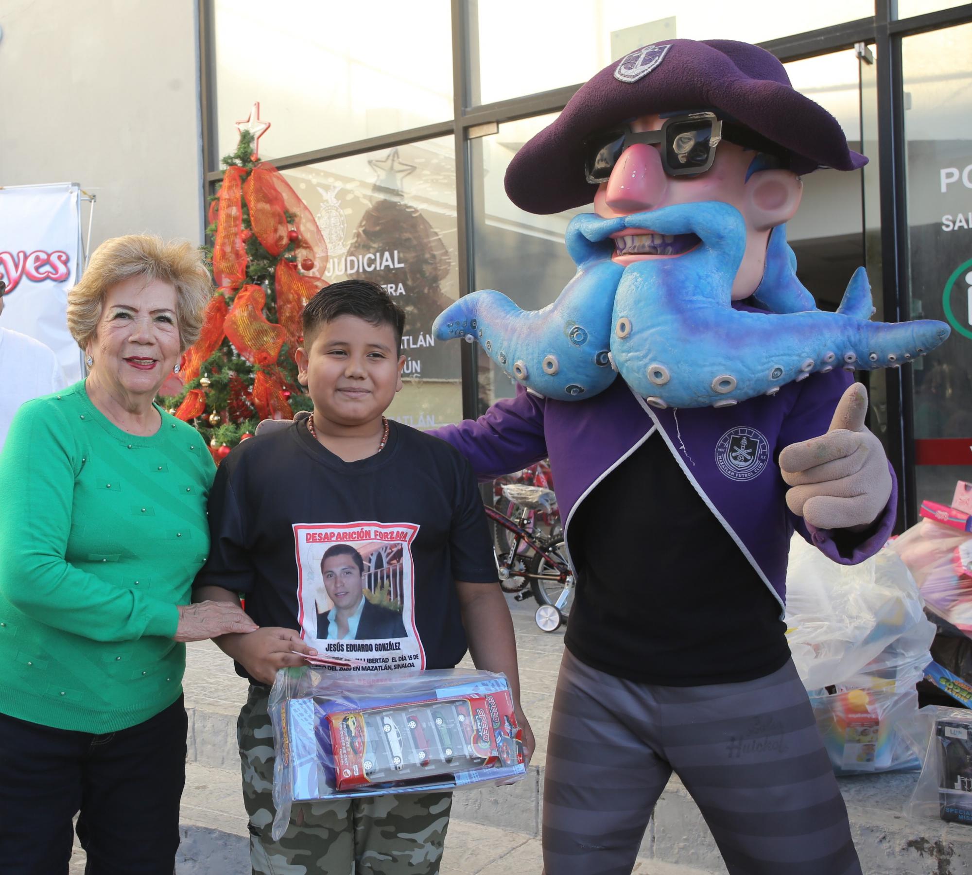 $!Lucy Calleros de Soto, responsable del área de espiritualidad y moral de la Unidad Noroeste de Anspac Mazatlán, hace entrega de un obsequio a Sergio Alejandro, quien quiere ser sacerdote, aquí junto a el Capitán Krak.