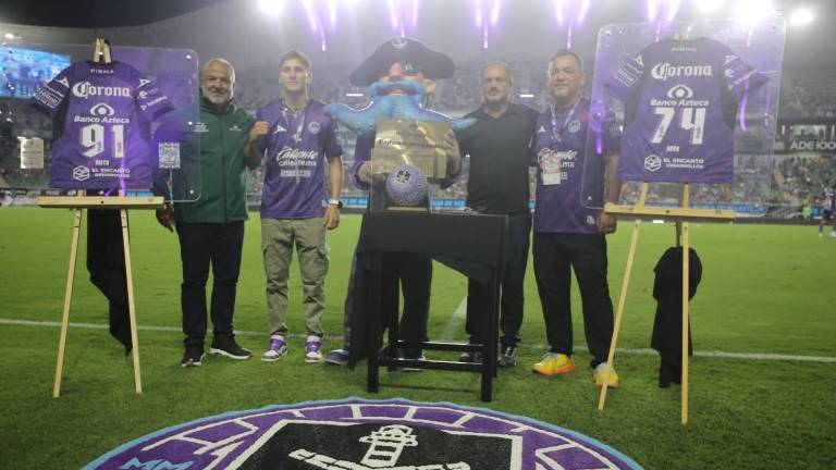 Marco Verde y Radamés Hernández muestran sus playeras moradas conmemorativas.