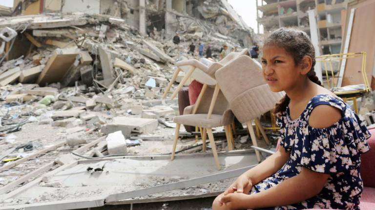 Una niña sentada entre los escombros de edificios destruidos en Gaza.